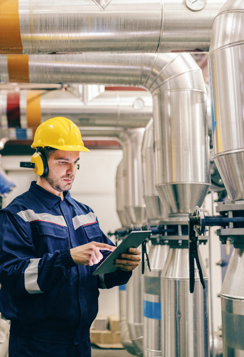 Young Caucasian man in protective suit using tablet while standing in heating plant